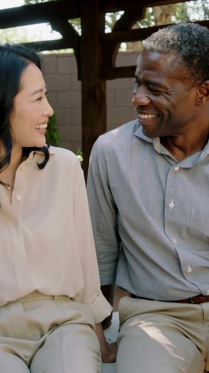 Vertical video: Smiling woman initiating smile, man laughing and leaning on pergola bench, bonding