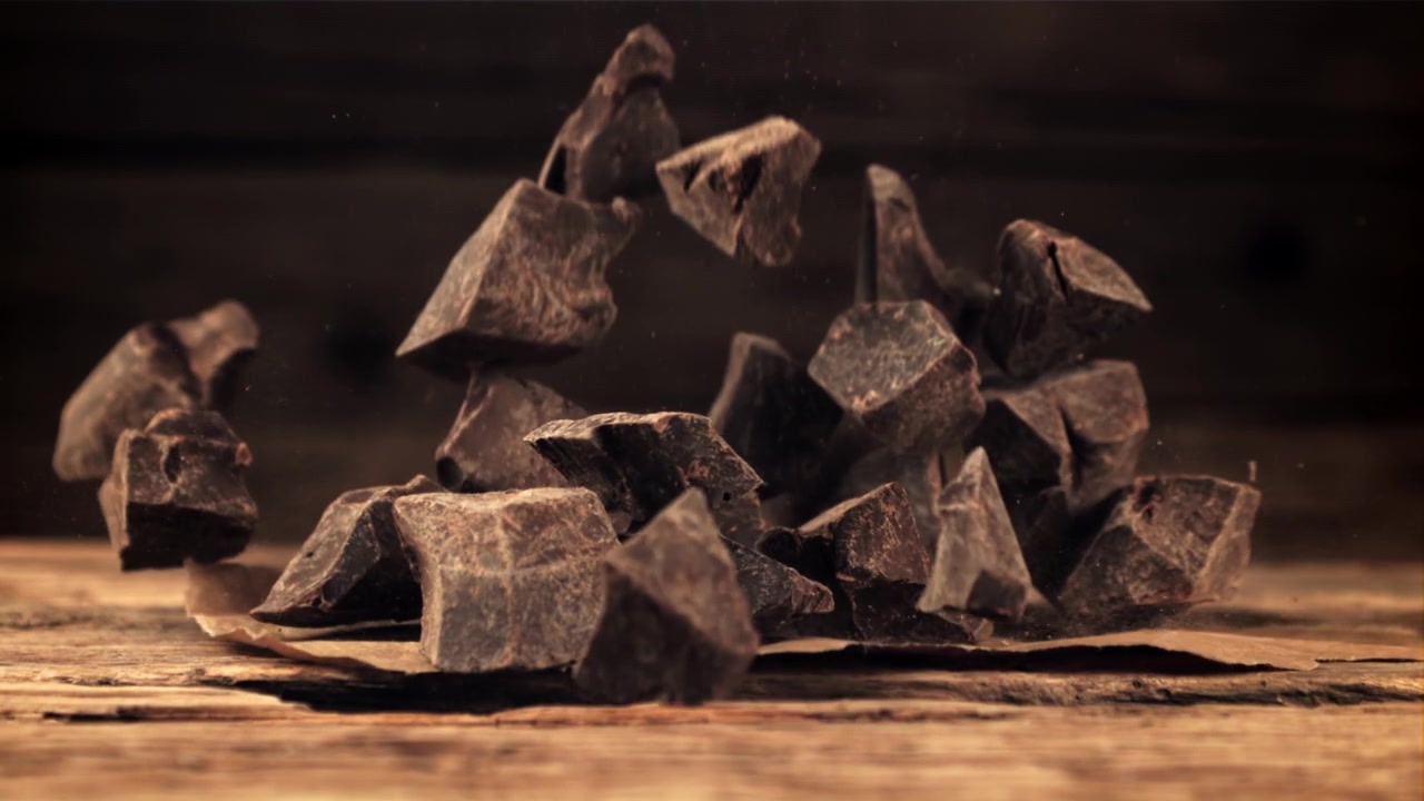Pezzi di cioccolato fondente che cadono al rallentatore su un tavolo di legno rustico