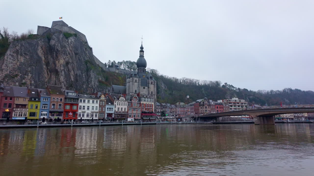 The collegiate church of our lady reflecting on the meuse river with colorful houses and a bridge