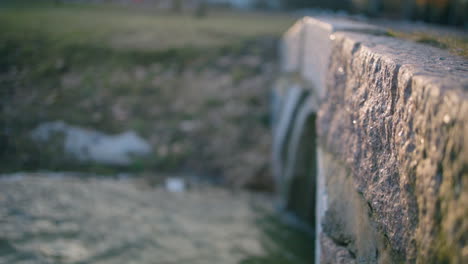 slomo pan of water flowing into sewage system with stone structure