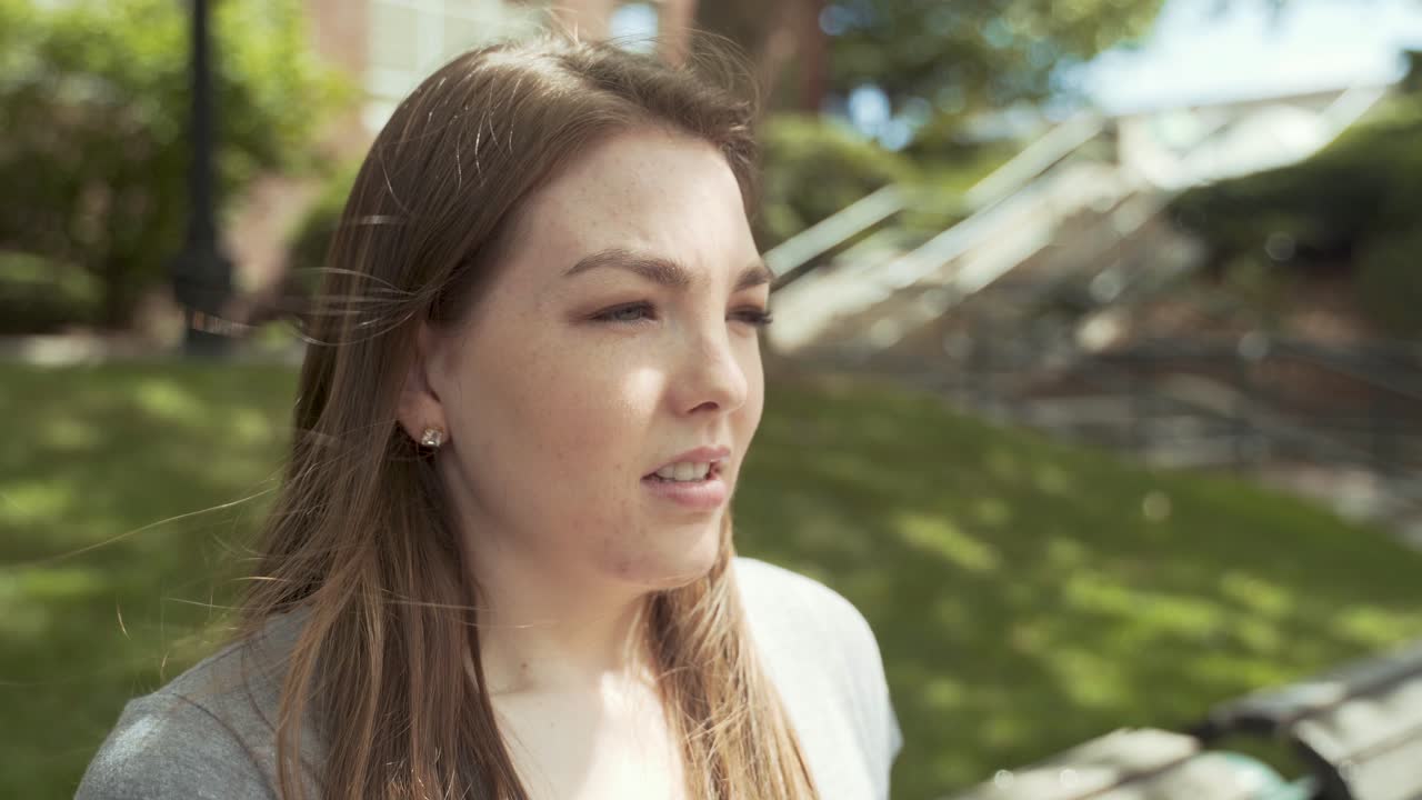 una joven blanca se quita la mascarilla para respirar aire fresco al aire libre en un banco del parque en un día soleado, con una foto de perfil lateral