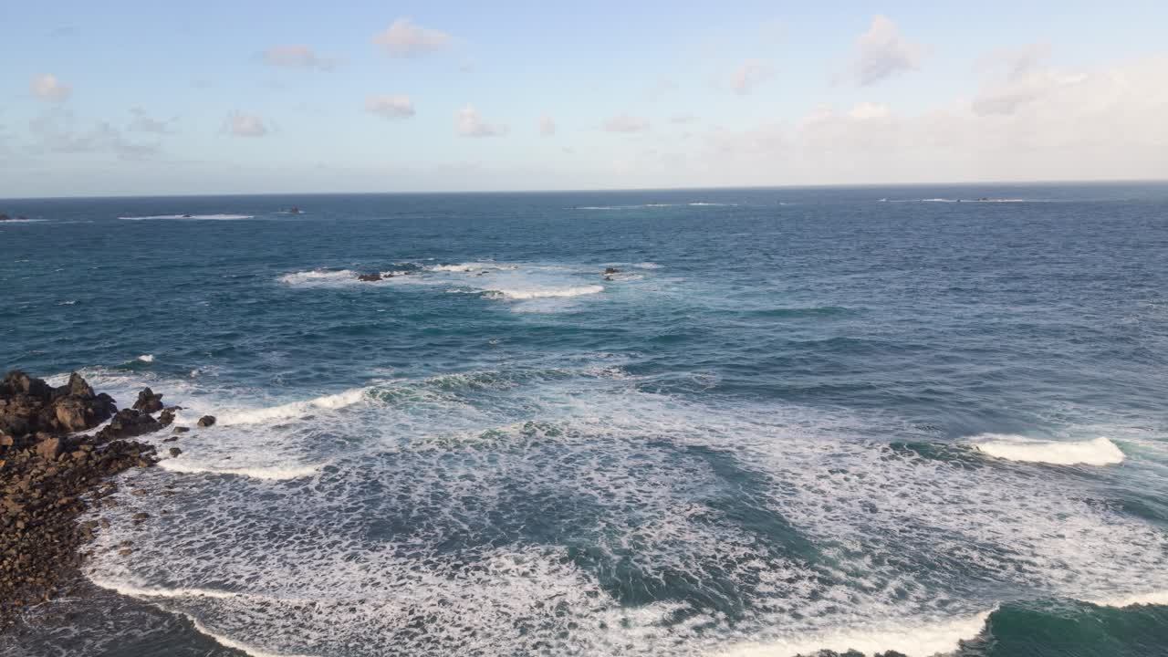 388 onde bianche spumeggianti che si infrangono a riva sotto il sole del tardo pomeriggio, con panoramica su un promontorio roccioso illuminato dal sole dorato e viste sul mare a Guernsey.