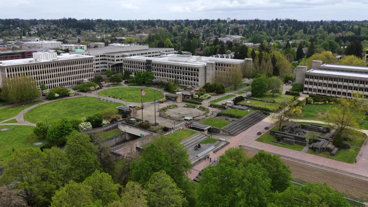Maestoso edificio assicurativo nel campus del Campidoglio dello Stato di Washington a Olympia, con bandiere americane e statali davanti all'architettura neoclassica negli USA. Ripresa aerea con drone in avvicinamento.