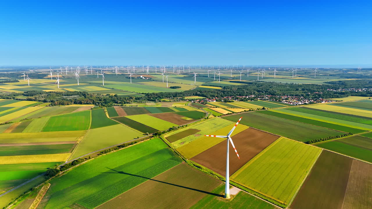 Green fields with wind turbines surrounding a little picturesque village. Green energy production concept. Aerial view.