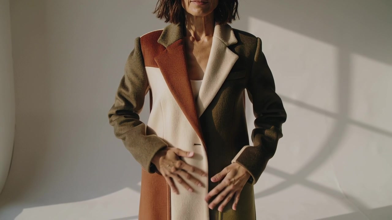 Donna che muove le braccia e sistema il cappotto colorblock in studio mentre la telecamera riprende mostrando le tasche