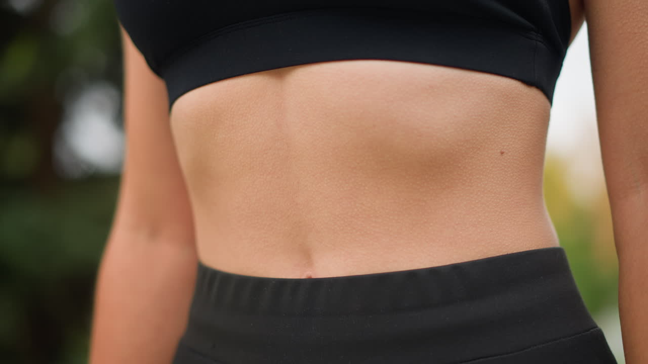 Close-up view of a woman's stomach with goosebumps as she breathes in deeply, showing her physical response to a deep breath while wearing black workout gear, focusing on her midsection