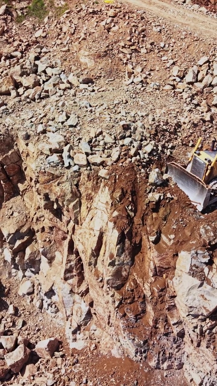 Bulldozer al lavoro su terreno roccioso in un cantiere edile durante il giorno.