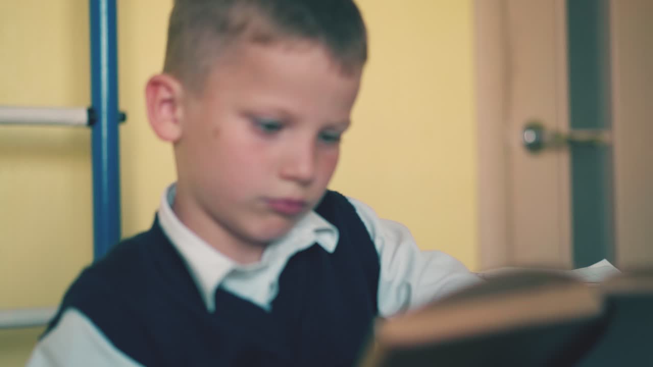 голубоглазый мальчик делает домашнее задание с учебниками за столом