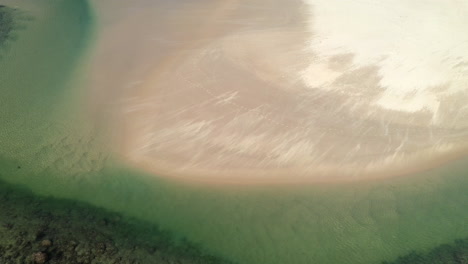 Rotating-drone-shot-of-wind-blowing-sand-across-a-sand-bar-at-Hat-Head-New-South-Wales,-Australia