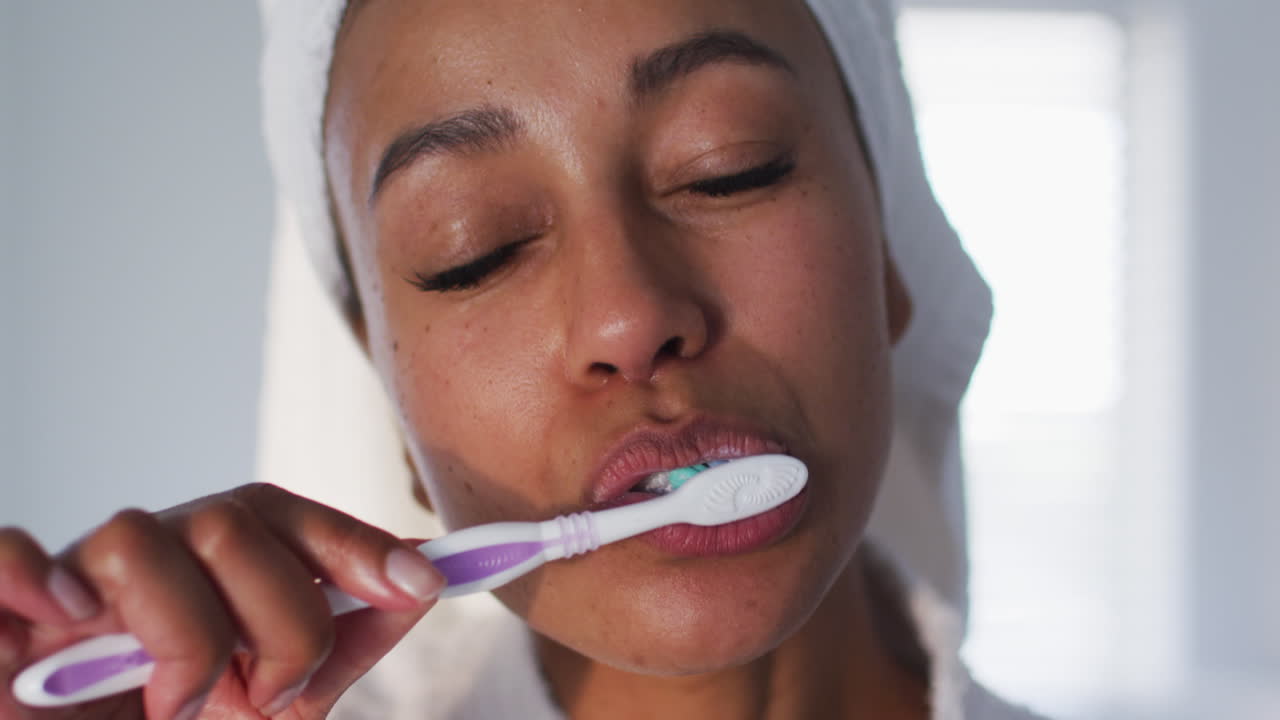 Portrait of african american woman in bathrobe brushing her teeth in the bathroom