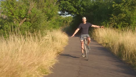 crazy young man riding a bicycle with no hands at dusk on a country road