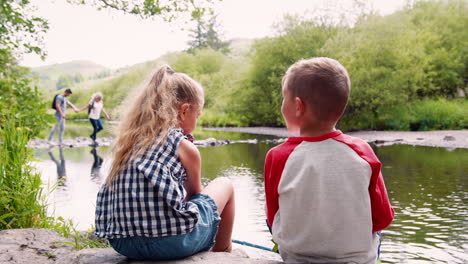 slow motion shot of children sitting on rocks fishing with nets in river in uk lake district