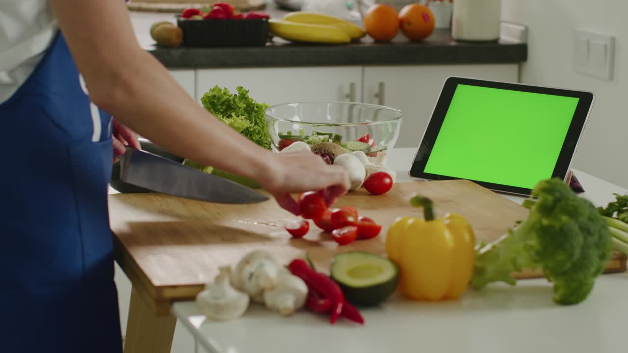 la mujer está cortando tomates cereza y mirando la tableta. tableta con pantalla verde. preparación de ensalada. 4k