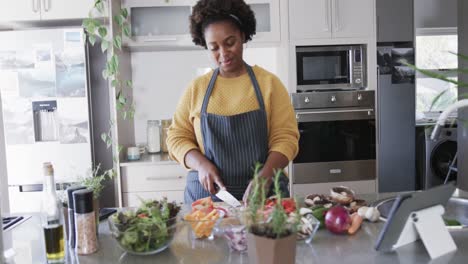 Happy-african-american-woman-in-apron-chopping-vegetables-in-kitchen,-slow-motion