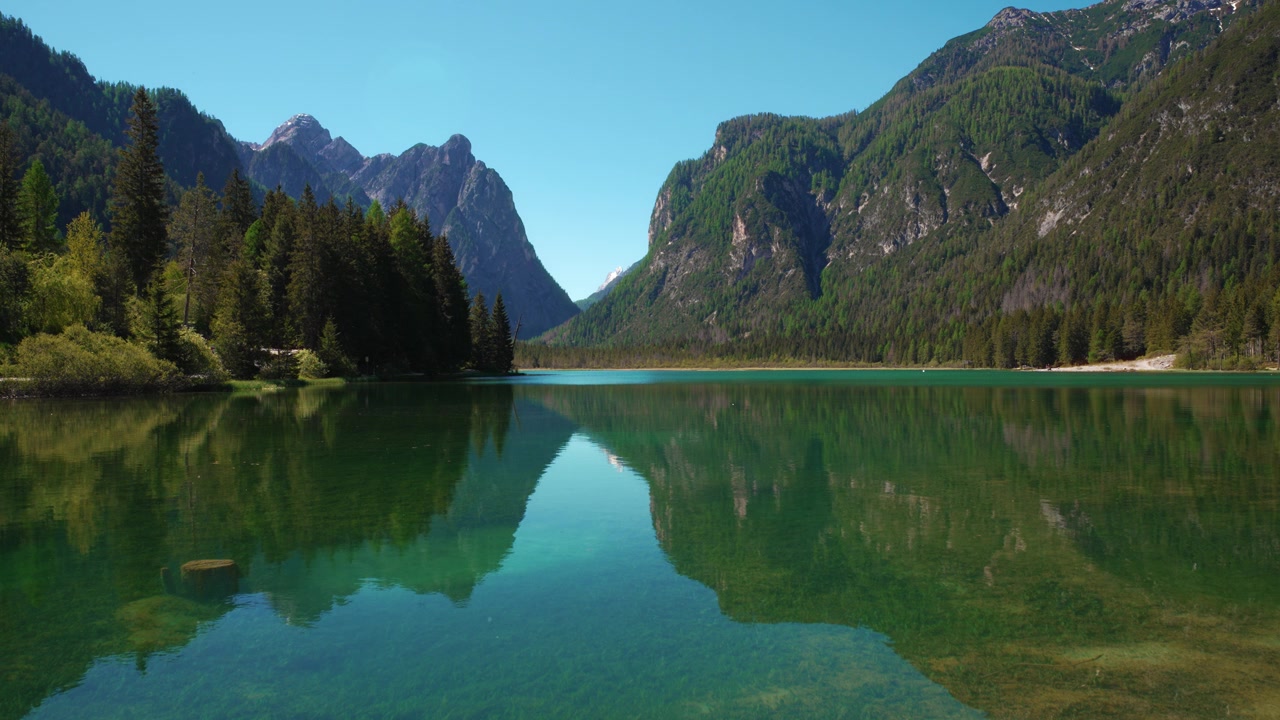 Vista serena sul limpido lago di montagna di Dobbiaco in Alto Adige verso le cime delle Dolomiti e le Tre Cime di Lavaredo