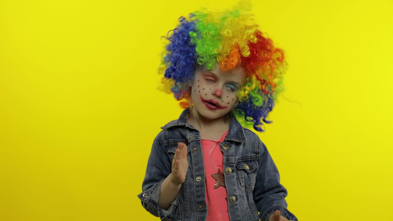 niña payaso en peluca haciendo caras tontas. divirtiéndose, muestra los movimientos del mimo. halloween