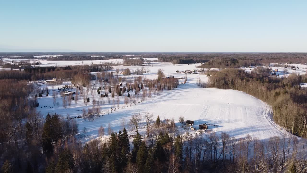 A wide shot of Latvia’s winter landscape, showcasing vast snow-covered fields, trees, and serene surroundings under a crisp, clear sky.