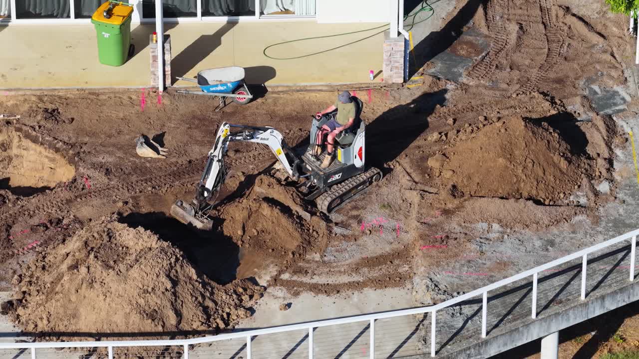 Drone captures excavator moving earth at a construction site under bright daylight in Gold Coast, Australia