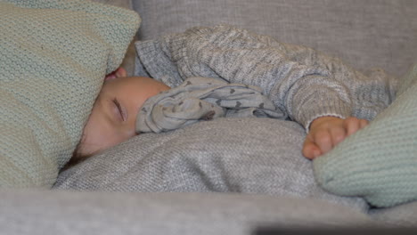 small child sleeps peacefully on couch with cushions around his head