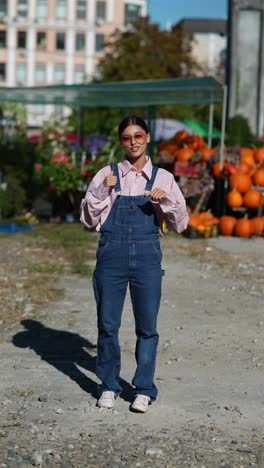 woman in pink shirt and denim overalls at a pumpkin patch