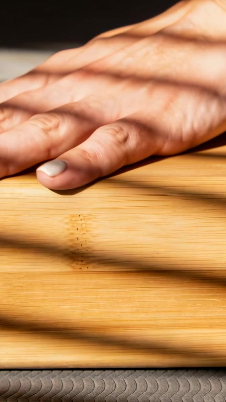 Vertical video: Placing hand sliding off wood board at window, blind shadows and white chipped nail