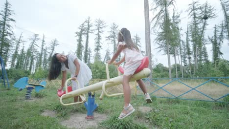 a pregnant mother and her young daughter enjoy playful time together at a playground in the park, surrounded by trees and greenery