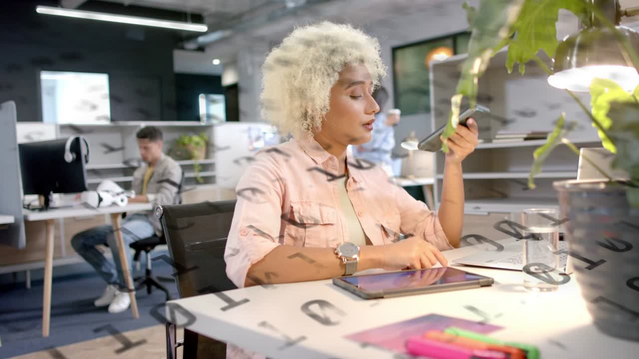Femme assise vérifiant son téléphone et tapotant sa tablette au bureau, lettres sur verre transparent, gérant des tâches.