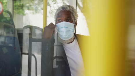 hombre mayor afroamericano con máscara facial hablando en un teléfono inteligente mientras estaba sentado en el autobús
