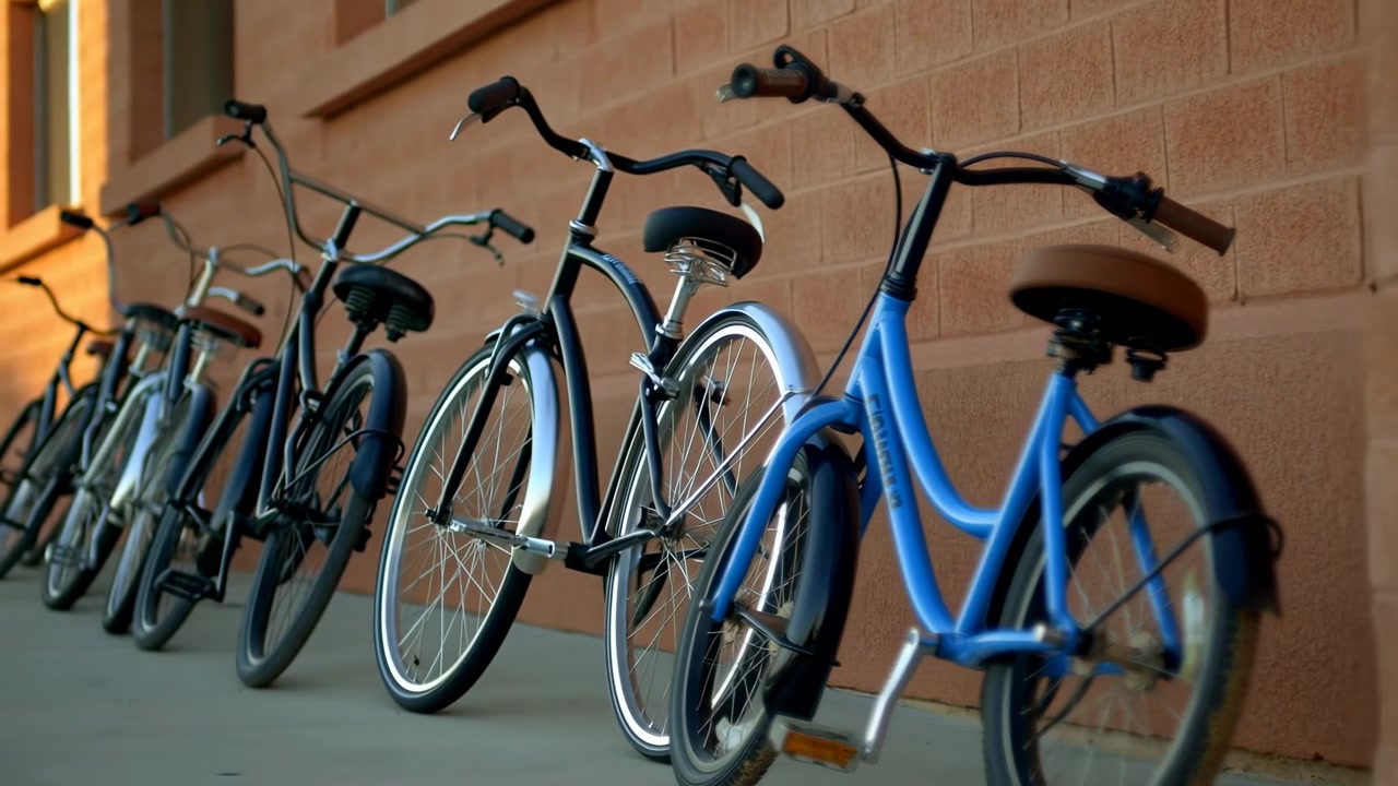 Multiple cruiser bicycles parked in neat row against textured tan brick wall, rightmost bright blue bike is prominent with brown sprung saddle, black handlebars with brown grips, front fender, pedal