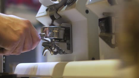 guy pouring coffee powder in a filter handle with a very fancy machine in a coffee shop