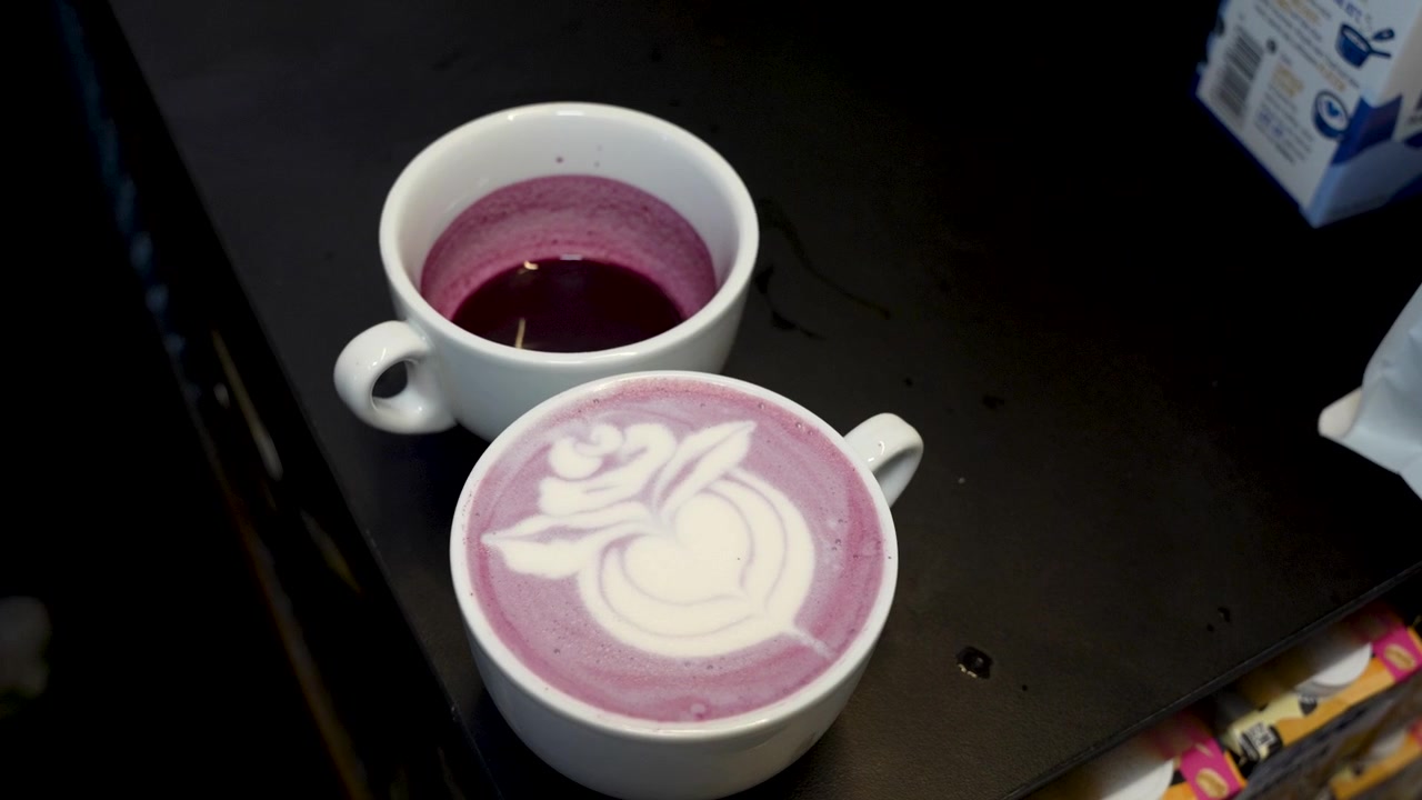 Purple ube latte with detailed floral foam art at a coffee festival in Ljubljana, Slovenia, showcasing colourful specialty cafe drink presentation, smooth cinematic close-up view