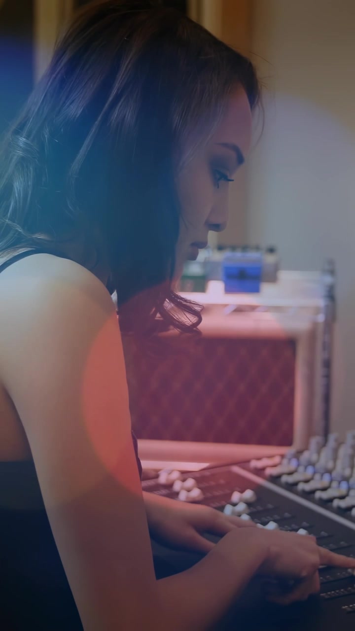 Video verticale: Tecnica audio donna che reagisce a una luce blu, regolando i fader per bilanciare il mix dello studio.