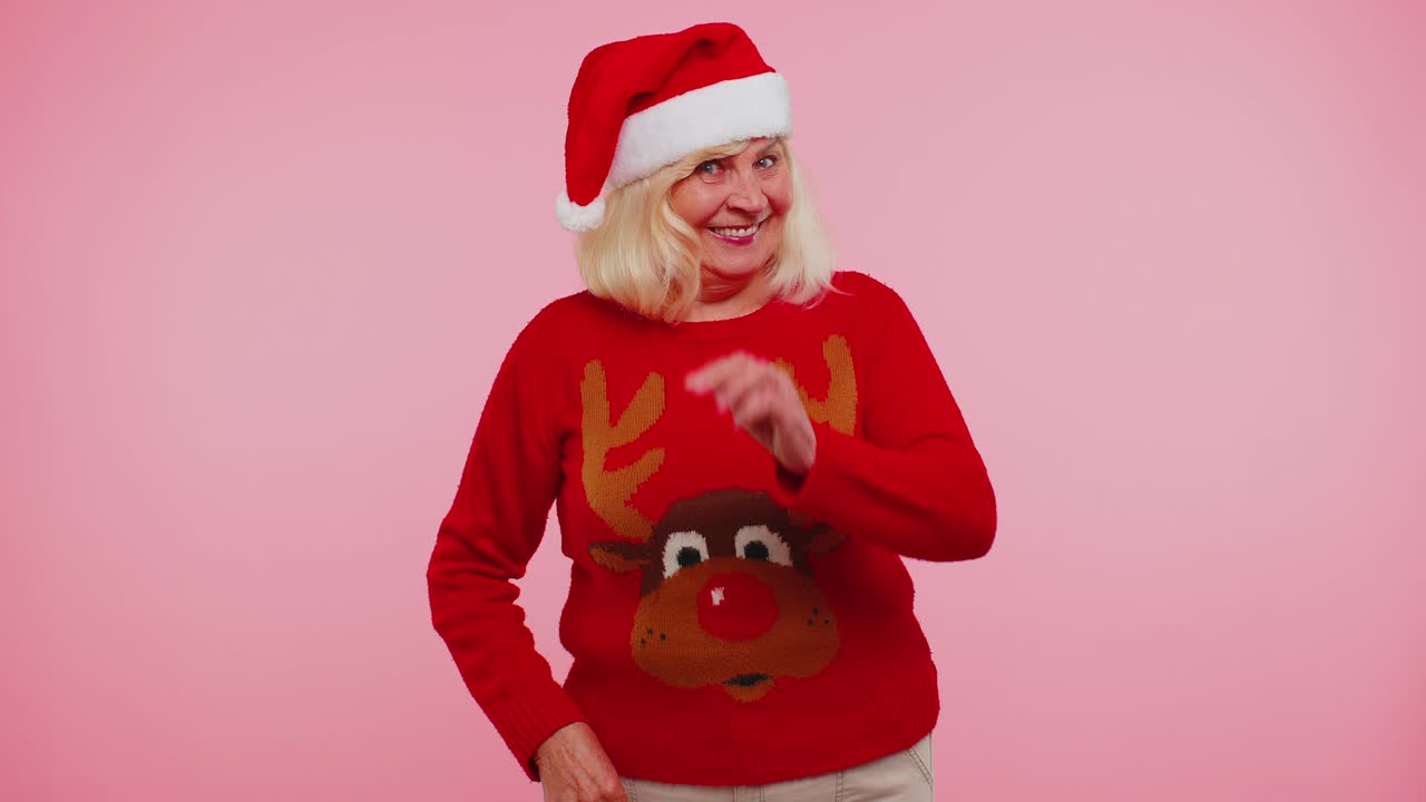 크리스마스 스웨터와 사을 입은 할머니 여성은 손바닥을 흔들며 인사 제스처로 누군가를 환영합니다.