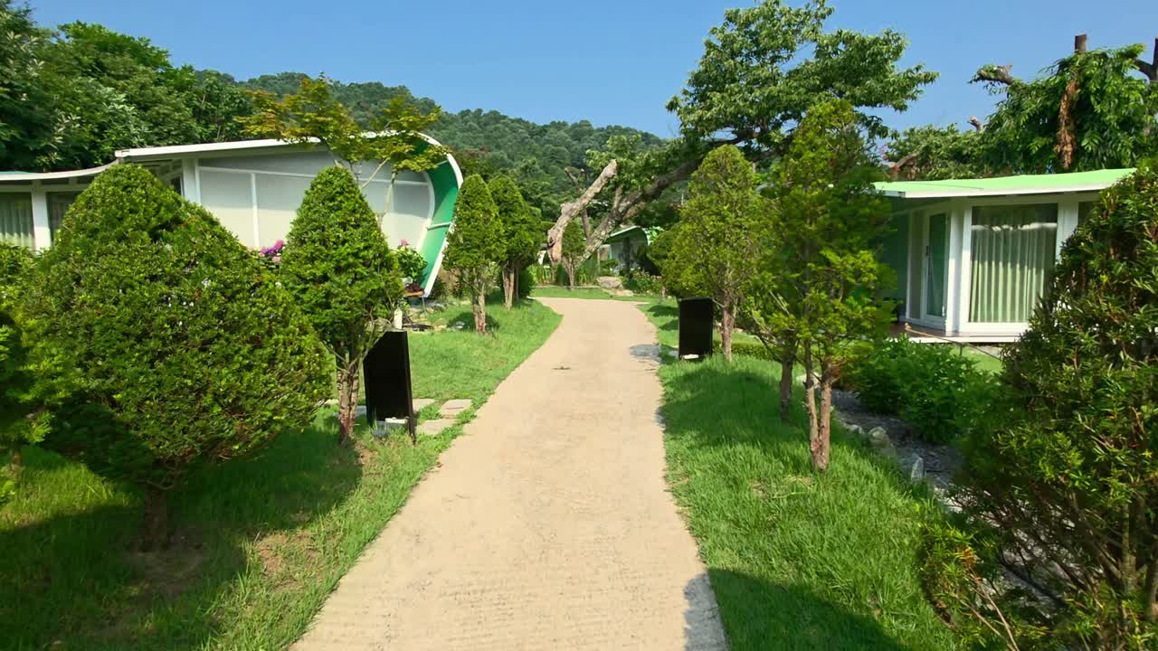 An immersive first-person point-of-view shot of a walk along a path at the Glam Tree resort in Gapyeong, South Korea, showing the unique, leaf-inspired modern architecture of the glamping cabins
