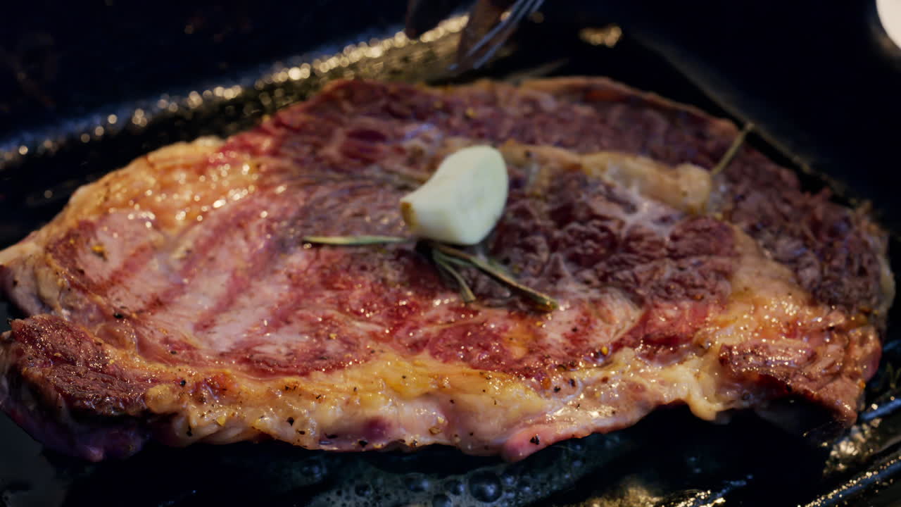 Burro che si scioglie su una bistecca condita che cuoce su una padella griglia calda con rosmarino
