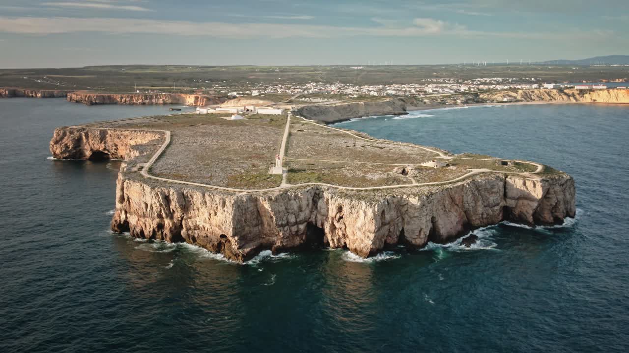 Dynamic aerial shot as drone performs a helix orbit around the cliffs at Sagres, capturing the lighthouse, fortress, and coastline of Portugal’s southwestern tip