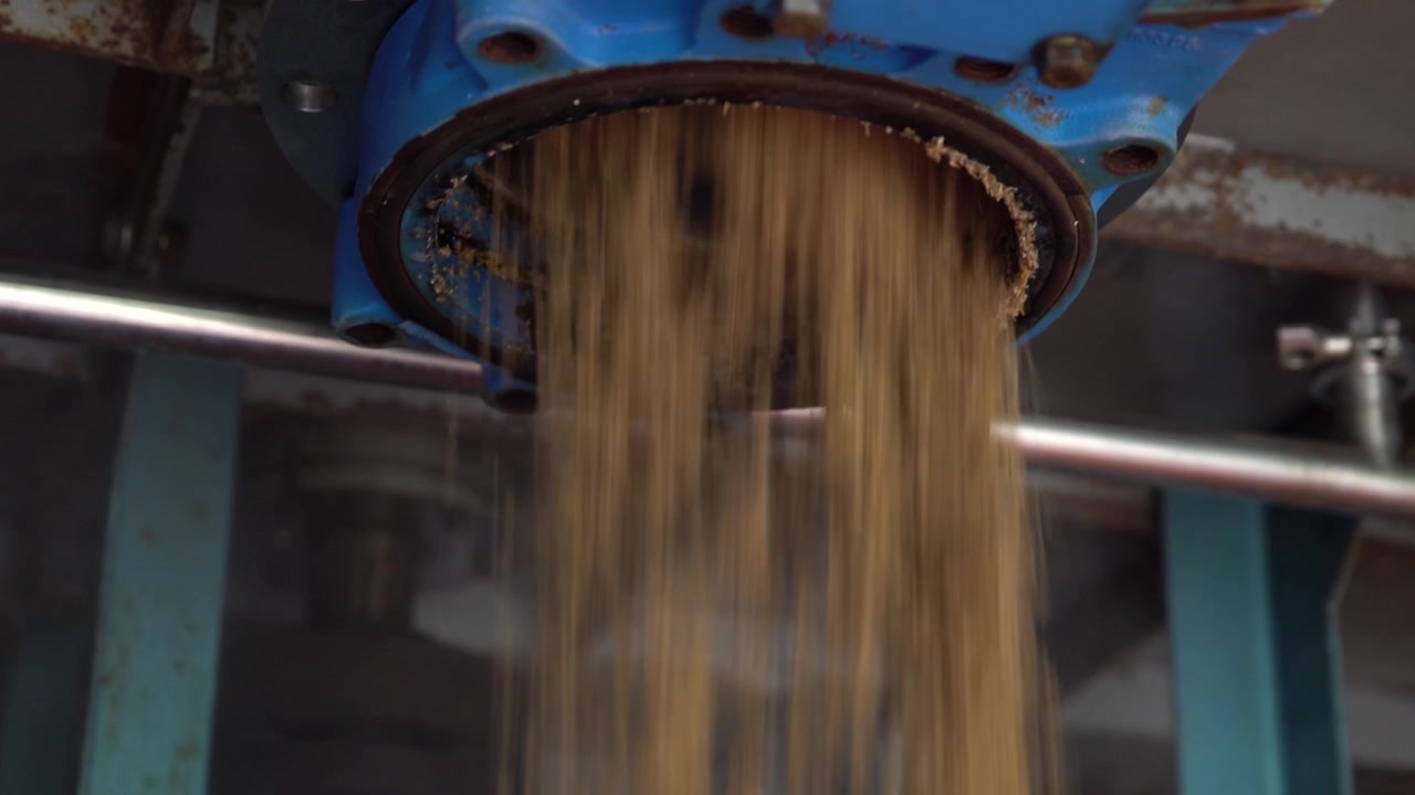 Grains falling out of a milling machine. Whole farming grains being crushed for processing. Brewing beer grains. Brewery grains being milled. Look up into the machine for a new look and angle.