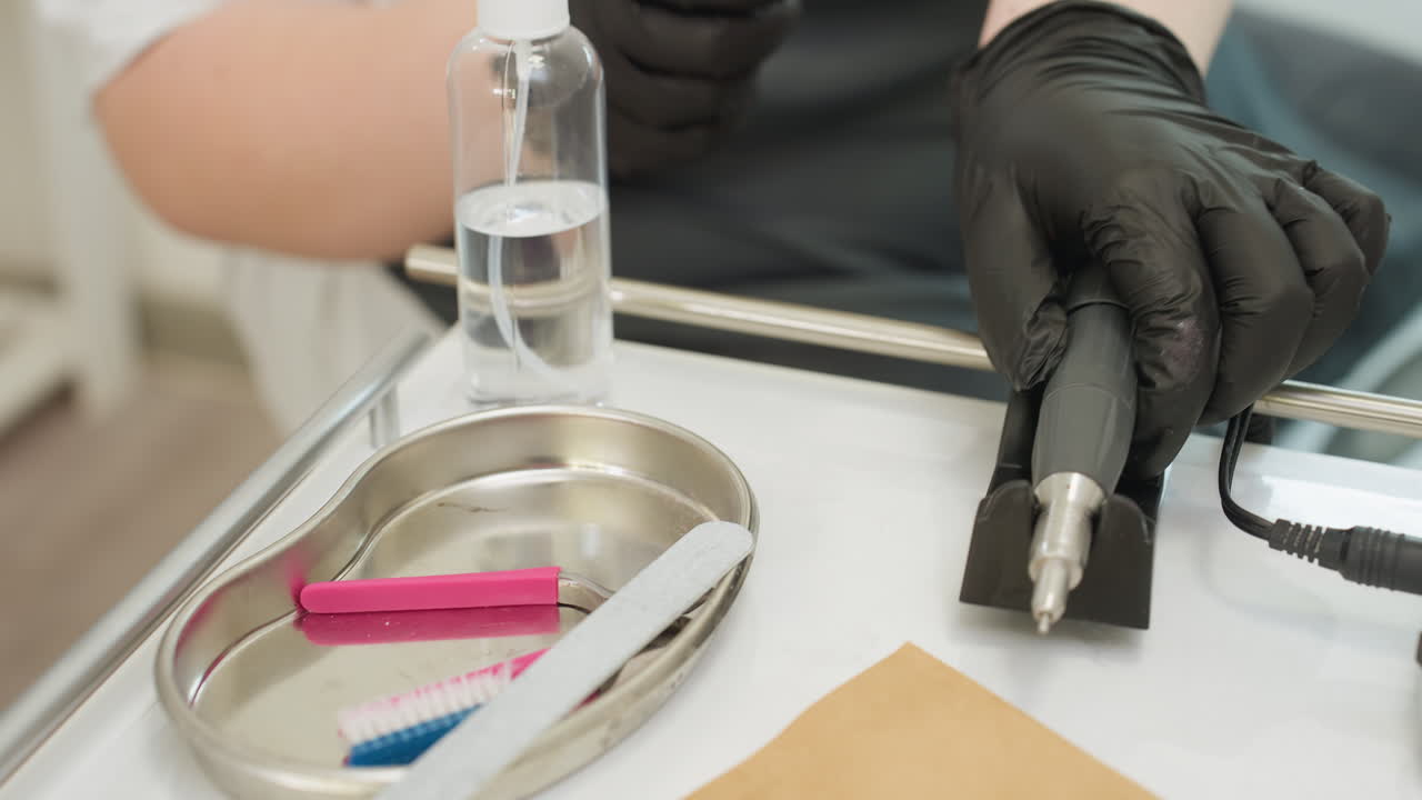 Close up of nail technician setting up electric filer next to stainless steel tray containing nail grooming tools and transparent spray bottle during professional manicure session in clean salon