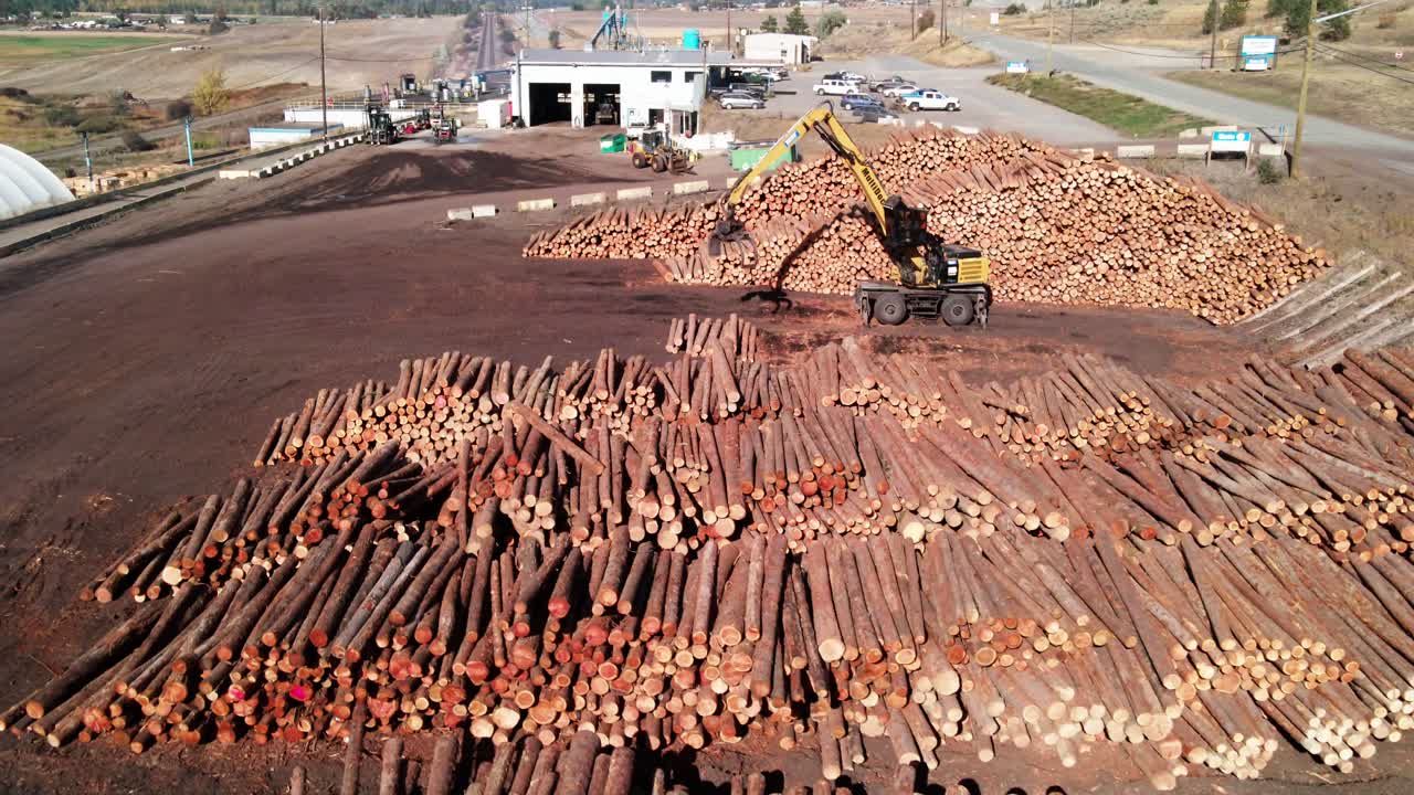 사막 환경에서 배경에 통나무 로더가 있는 제재소에서 통나무 더미의 돌리 거꾸로 드론 샷
