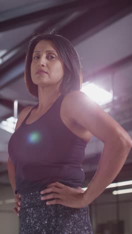 vertical video portrait of mature woman wearing fitness clothing standing in gym ready to exercise