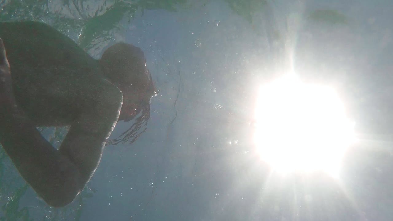 Vertical video, Young boy swimming underwater, low angle view, Camera look up towards Sunlight