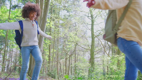 two children walking through bluebell woods in springtime balancing on log