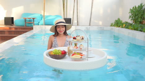 woman in sexy swimsuit sharing floating tray with coffee and exotic treat