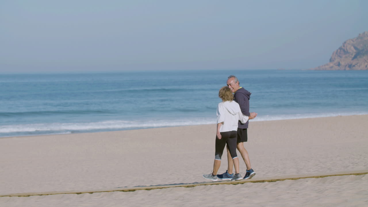 una feliz pareja madura cogida de las manos y caminando por la playa de arena