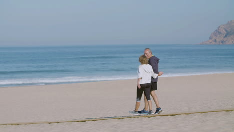 Happy-mature-couple-holding-hands-and-walking-on-sandy-beach