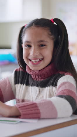 a young girl smiles happily while sitting at a desk in a classroom.