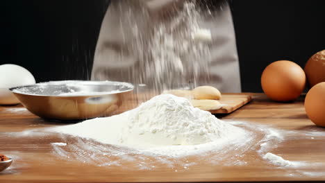 baking preparation with flour, eggs, and tools on wooden table. a person is pouring flour onto a wooden table, preparing for baking with eggs and utensils nearby.