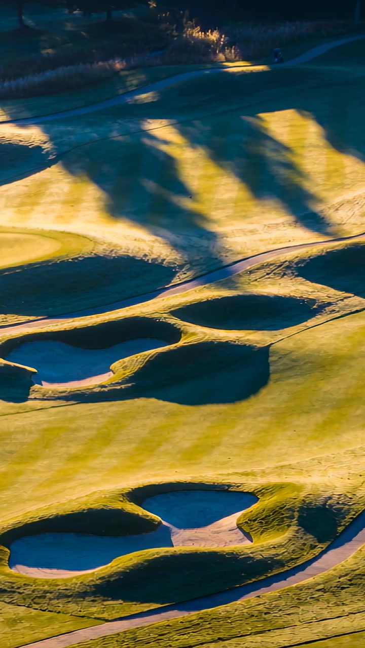 Verticale video: Panorerende drone begint veegbeweging, legt gebeeldhouwde bunkers en gestreepte fairway vast