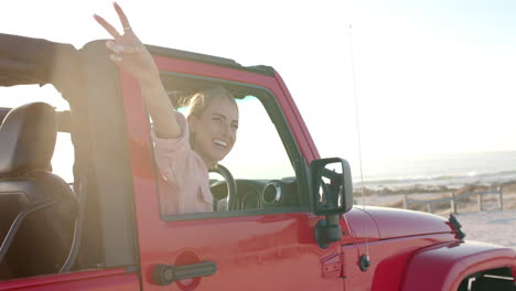 joven mujer caucásica disfruta de una playa soleada en un jeep rojo en un viaje por carretera