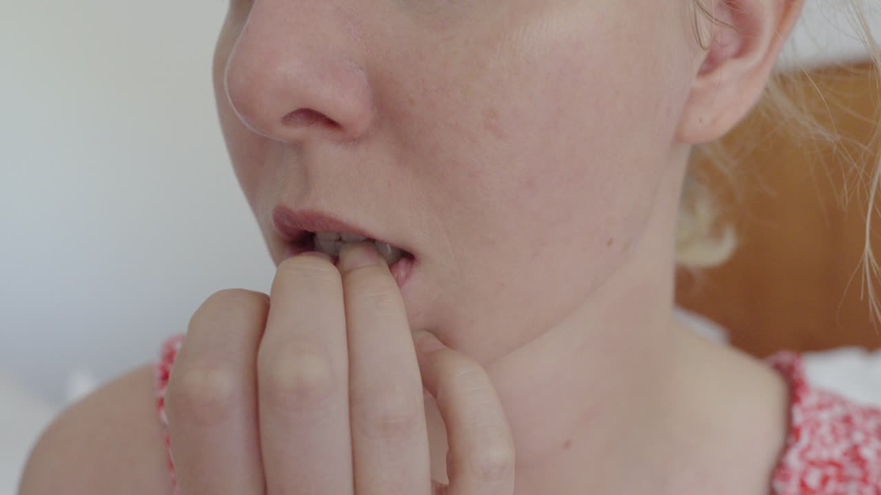 Close-up of a woman repeatedly biting her fingernails. The gesture highlights anxiety, stress or a compulsive tick, representing nervous behavior and unhealthy coping mechanisms